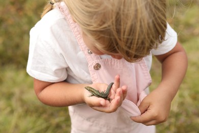 Little girl holding lizard on blurred background. Enjoying beautiful nature