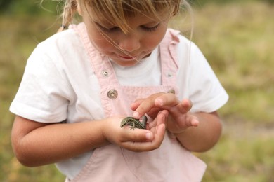 Photo of Little girl holding lizard on blurred background. Enjoying beautiful nature