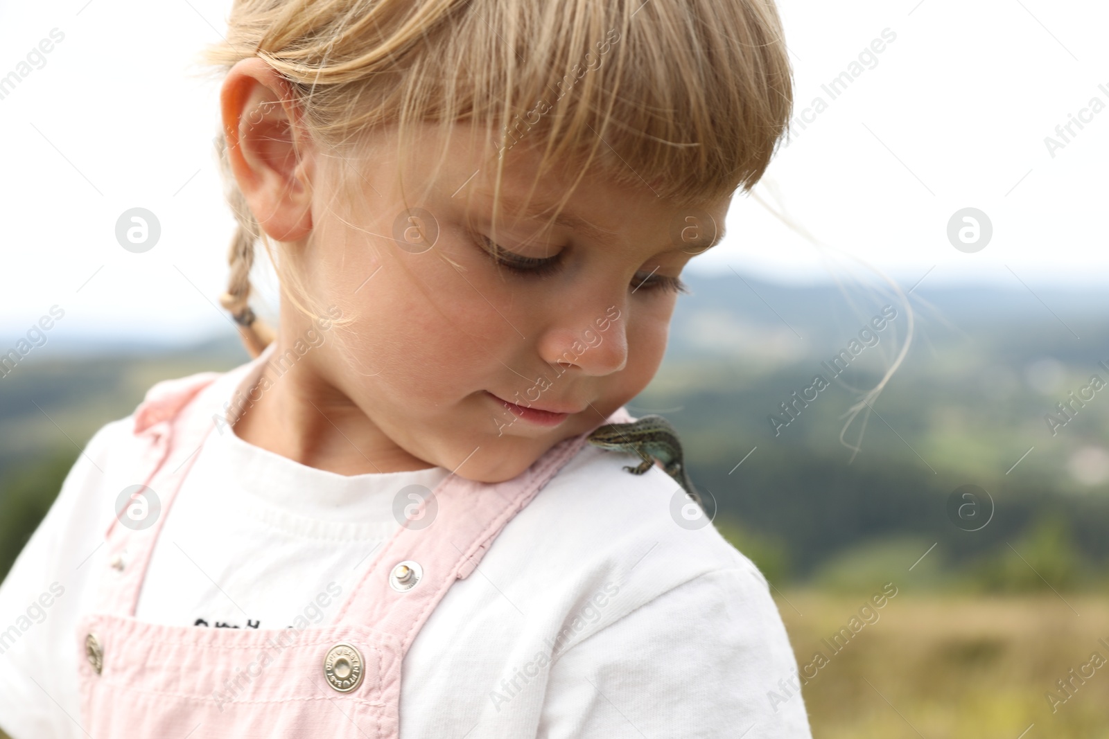 Photo of Cute little girl with lizard on shoulder outdoors. Enjoying beautiful nature