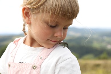 Cute little girl with lizard on shoulder outdoors. Enjoying beautiful nature