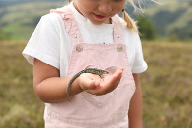 Little girl holding lizard on blurred background, closeup. Enjoying beautiful nature