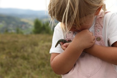 Photo of Cute little girl holding lizard at field, space for text. Enjoying beautiful nature