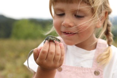 Little girl exploring lizard on blurred background. Enjoying beautiful nature