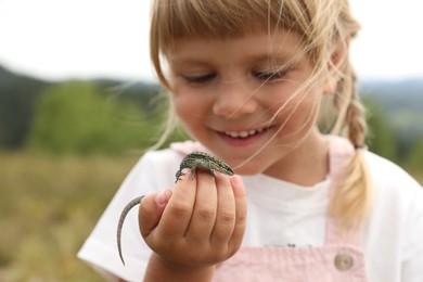 Smiling little girl exploring lizard on blurred background. Enjoying beautiful nature