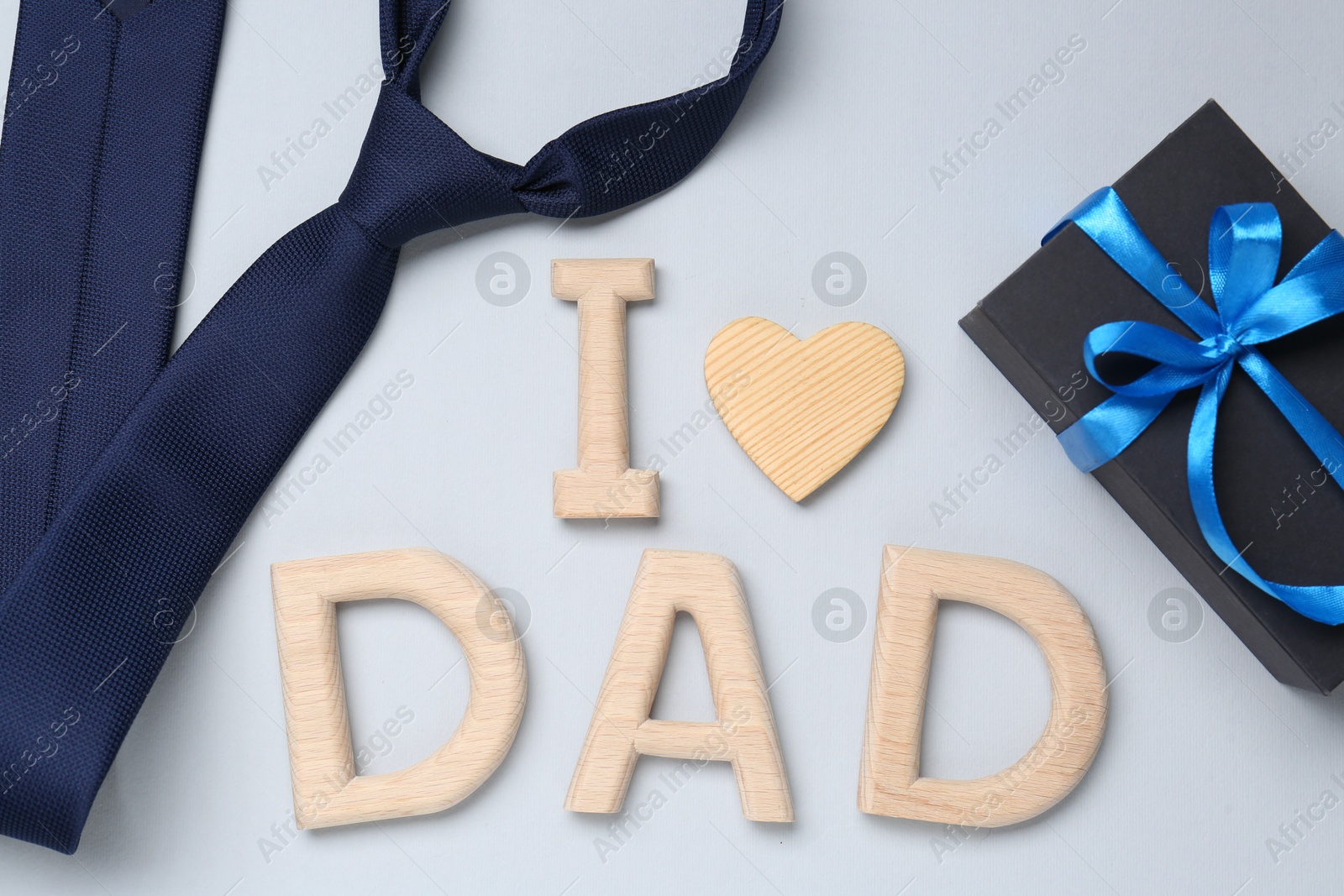 Photo of Happy Father's Day. Phrase I love Dad made with wooden letters, gift and tie on light background, flat lay