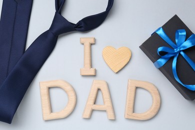 Photo of Happy Father's Day. Phrase I love Dad made with wooden letters, gift and tie on light background, flat lay