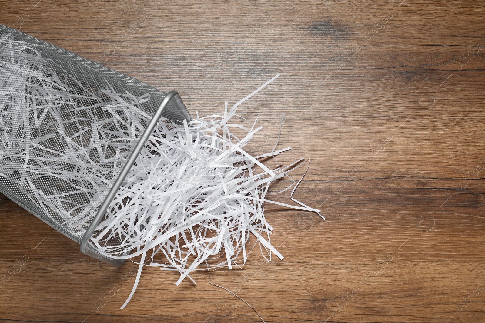 Photo of Shredded paper strips in trash bin on wooden table, top view. Space for text