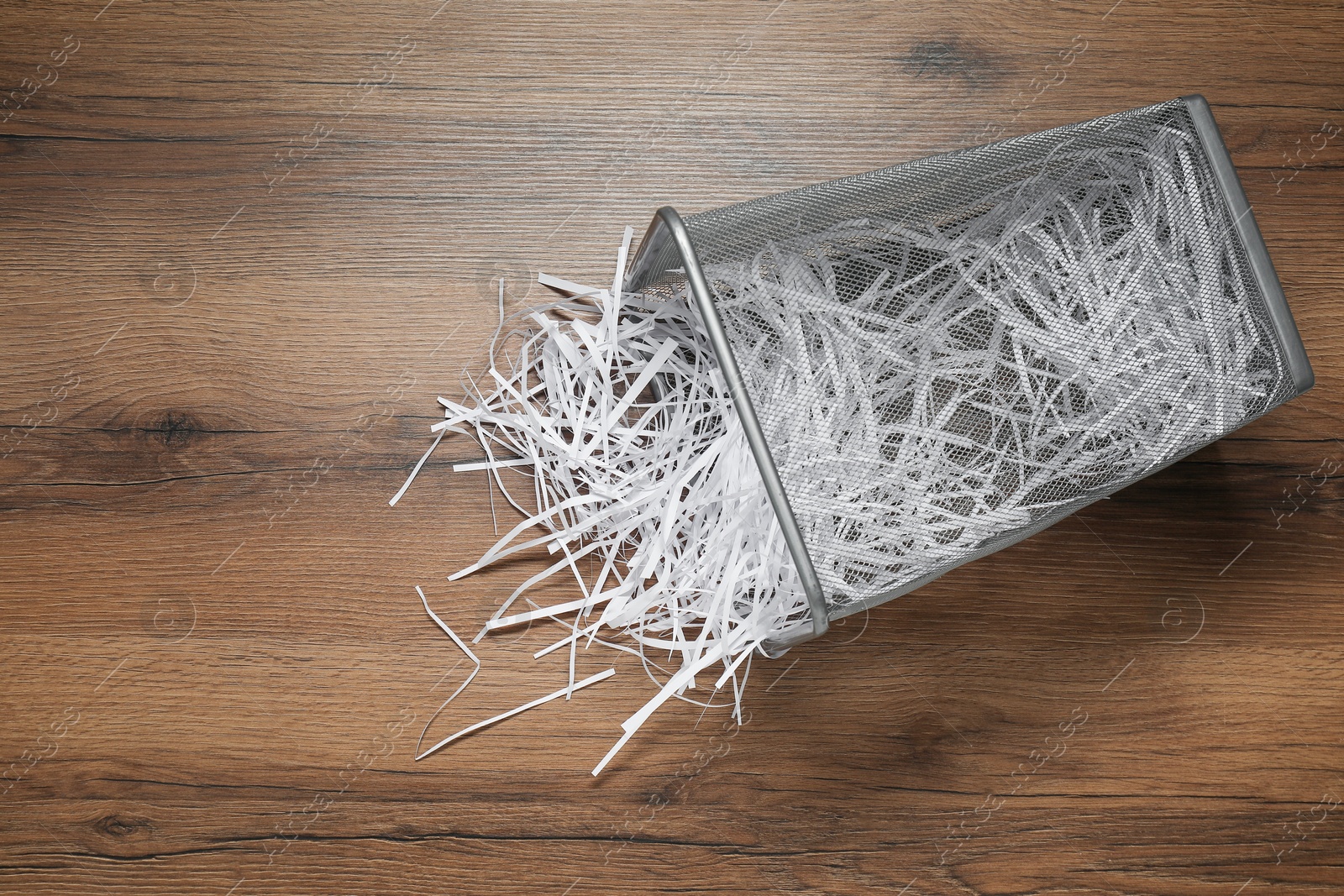 Photo of Shredded paper strips in trash bin on wooden table, top view