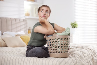 Tired housewife with basket full of laundry on bed at home