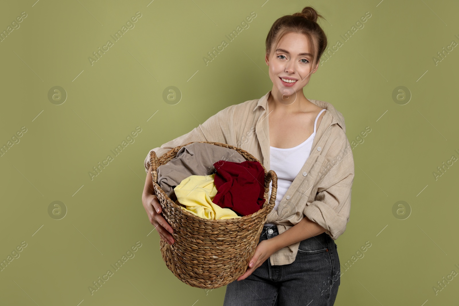 Photo of Happy young housewife with basket full of laundry on olive background