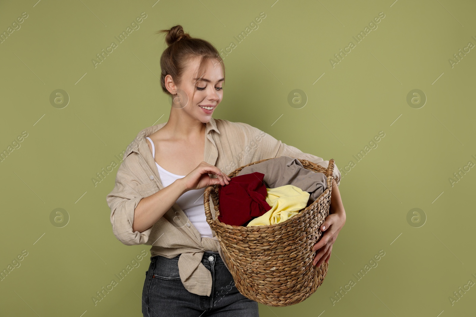 Photo of Happy young housewife with basket full of laundry on olive background