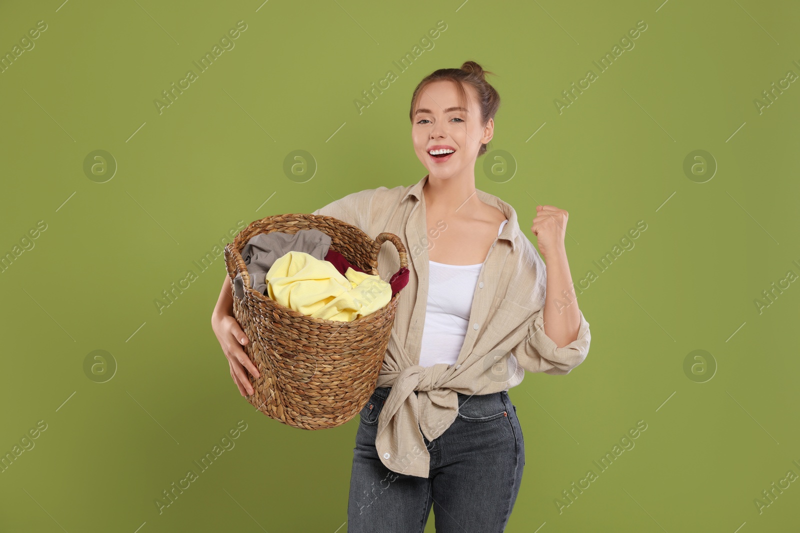 Photo of Happy young housewife with basket full of laundry on olive background