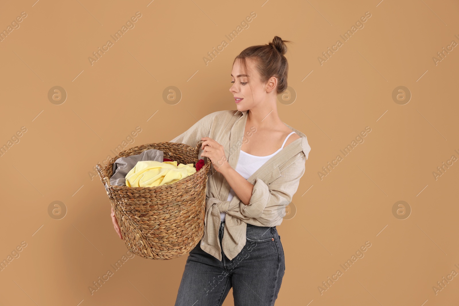 Photo of Happy housewife with basket full of laundry on pale orange background