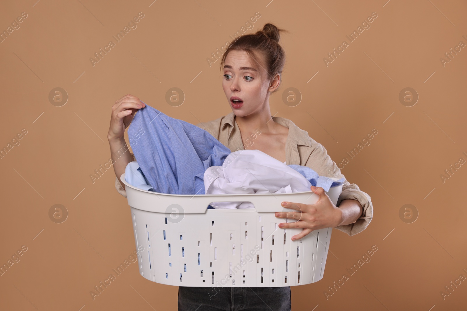 Photo of Emotional housewife with basket full of laundry on pale orange background