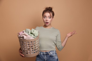 Photo of Emotional housewife with basket full of laundry on pale orange background