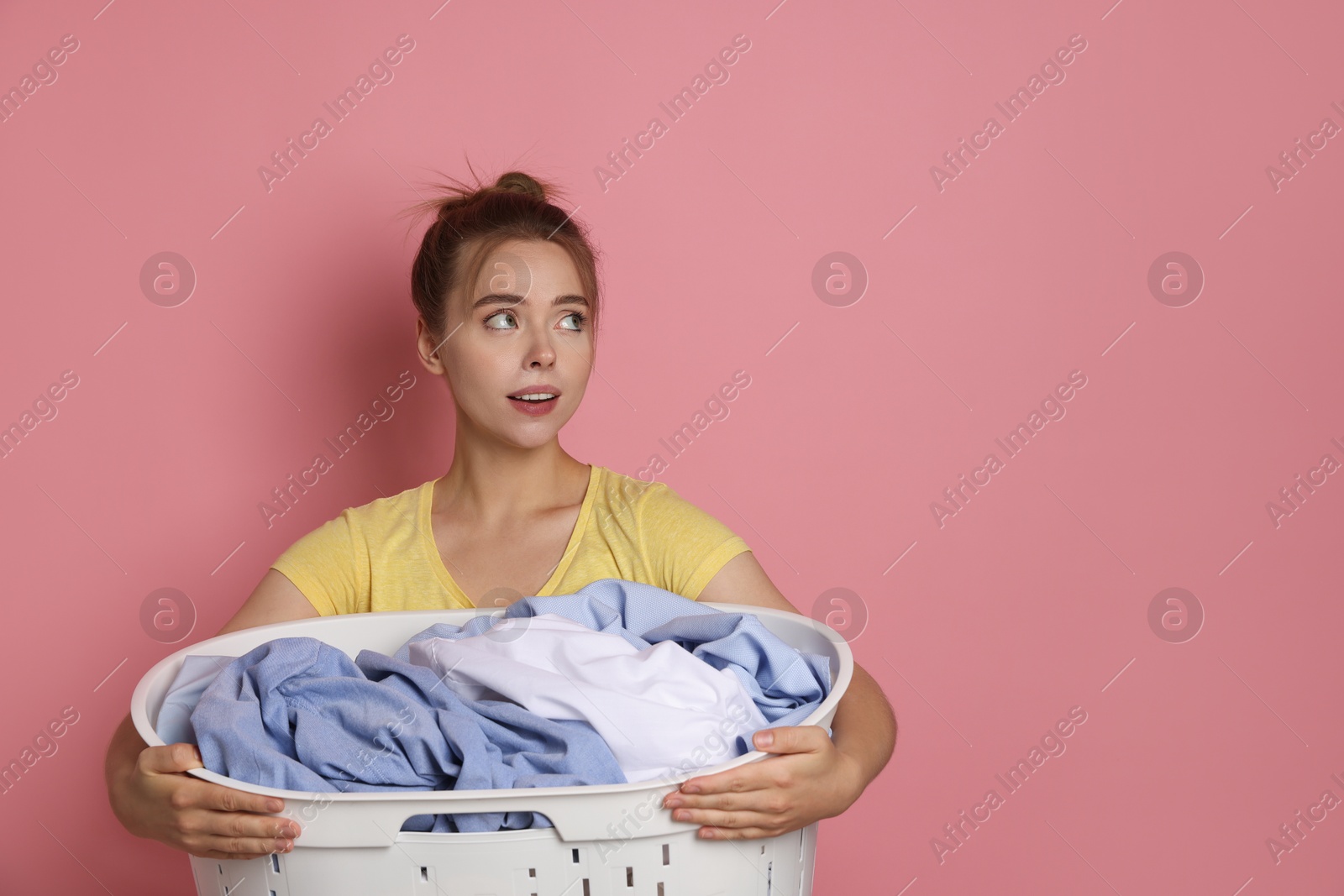 Photo of Young housewife with basket full of laundry on pale pink background. Space for text