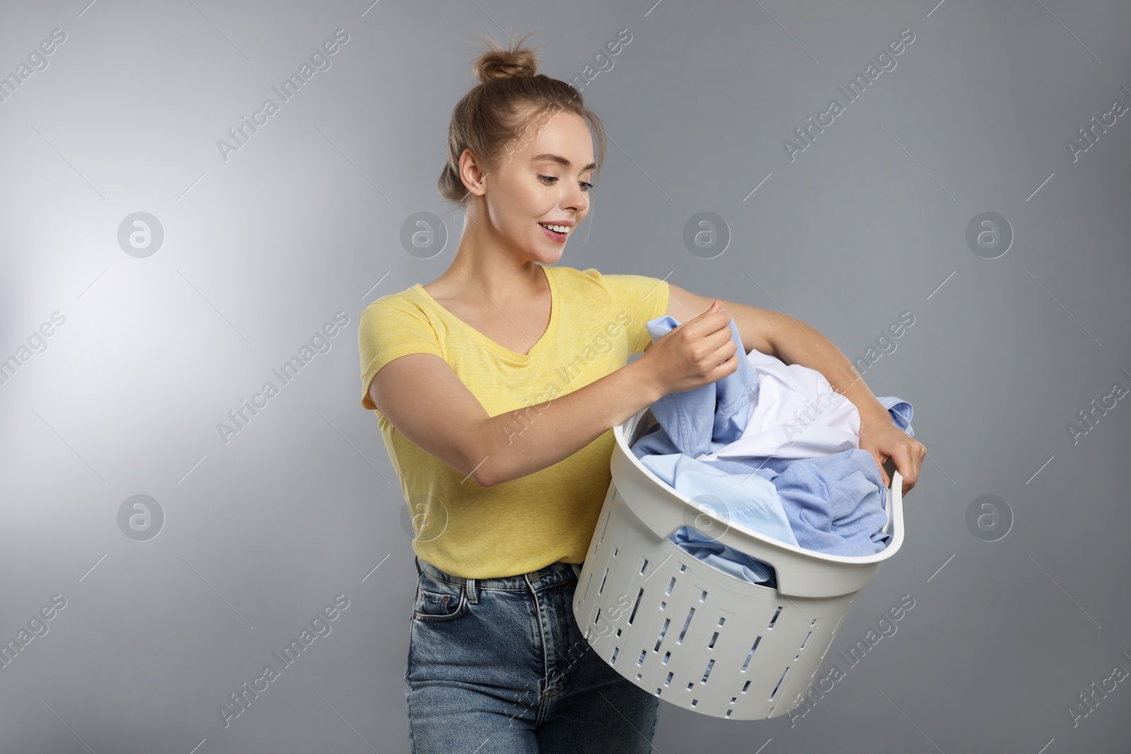 Photo of Happy young housewife with basket full of laundry on grey background