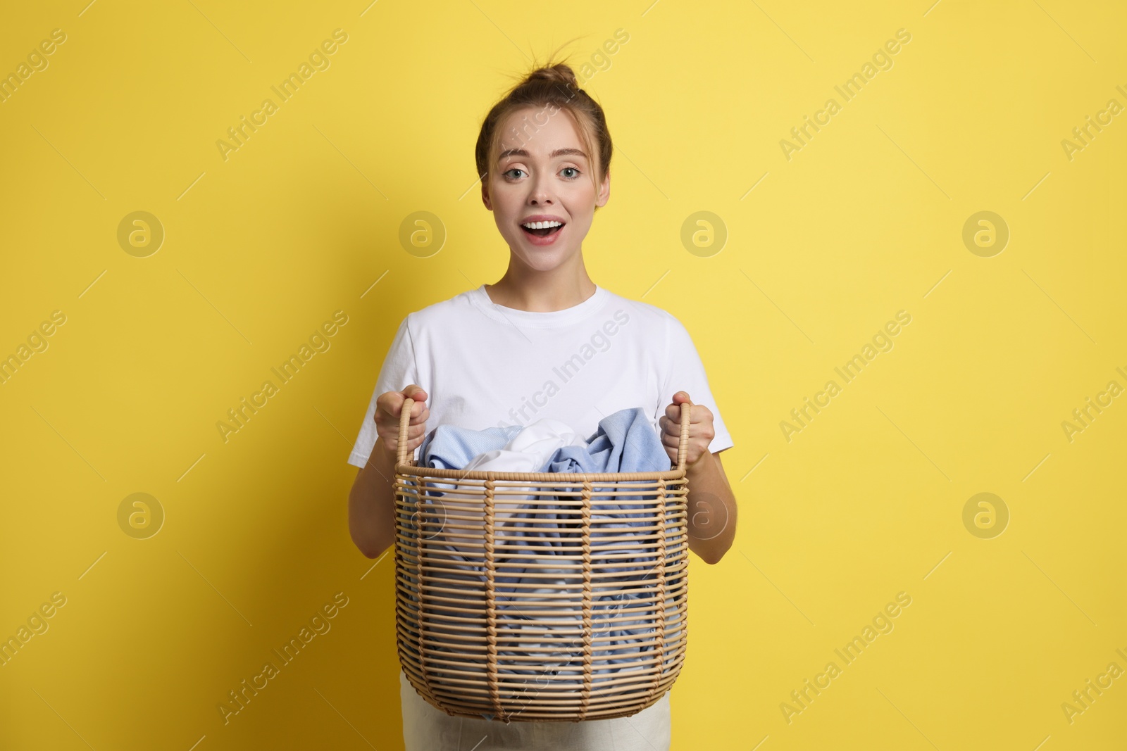 Photo of Happy young housewife with basket full of laundry on yellow background