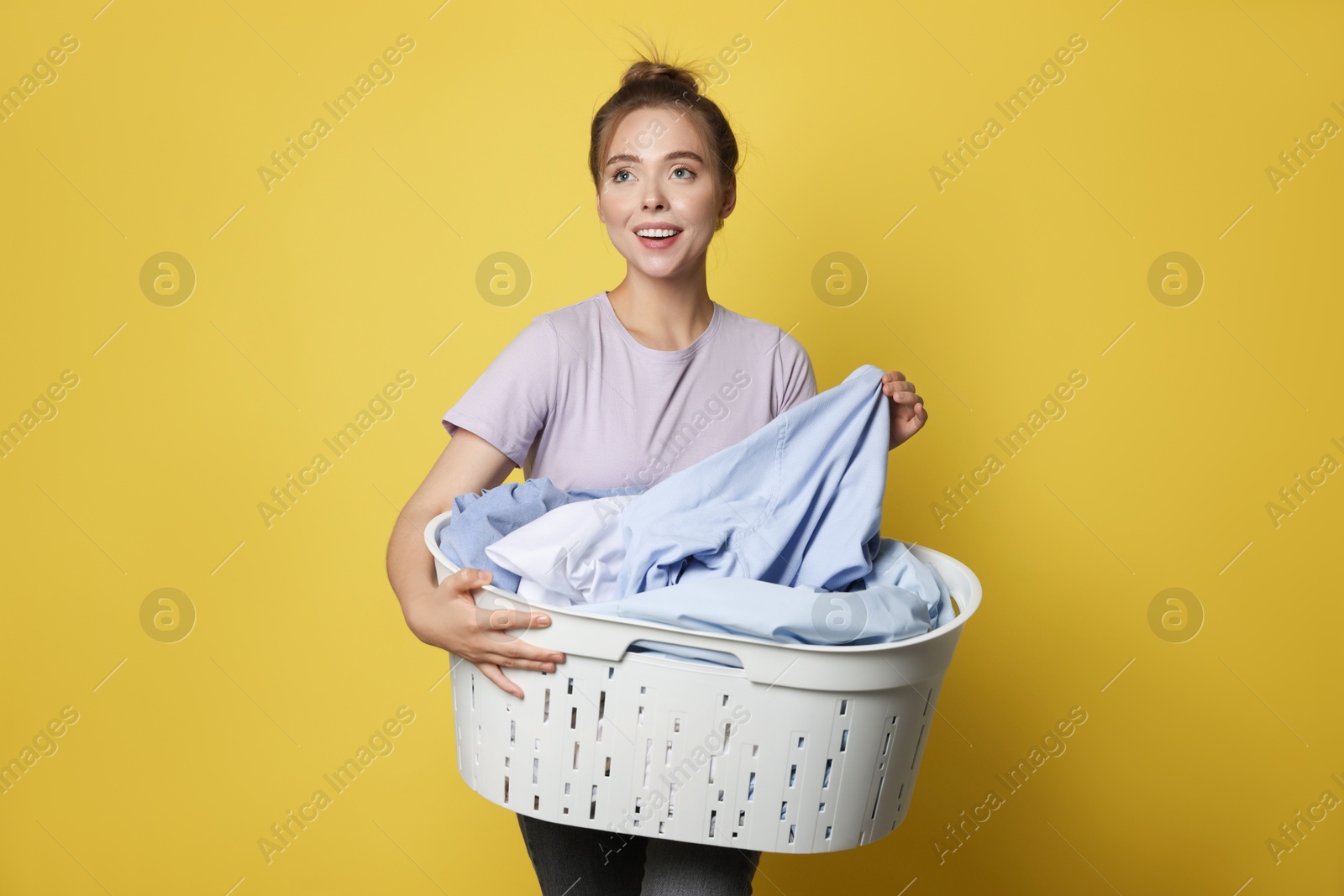 Photo of Happy young housewife with basket full of laundry on yellow background