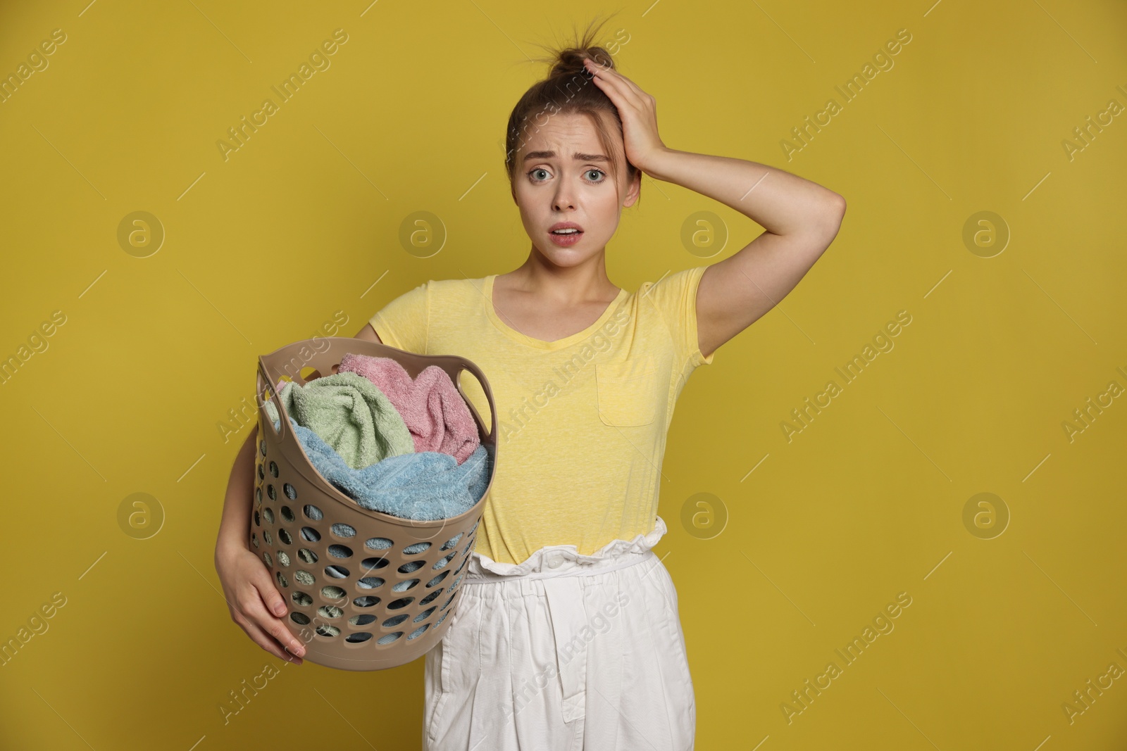 Photo of Tired housewife with basket full of laundry on yellow background