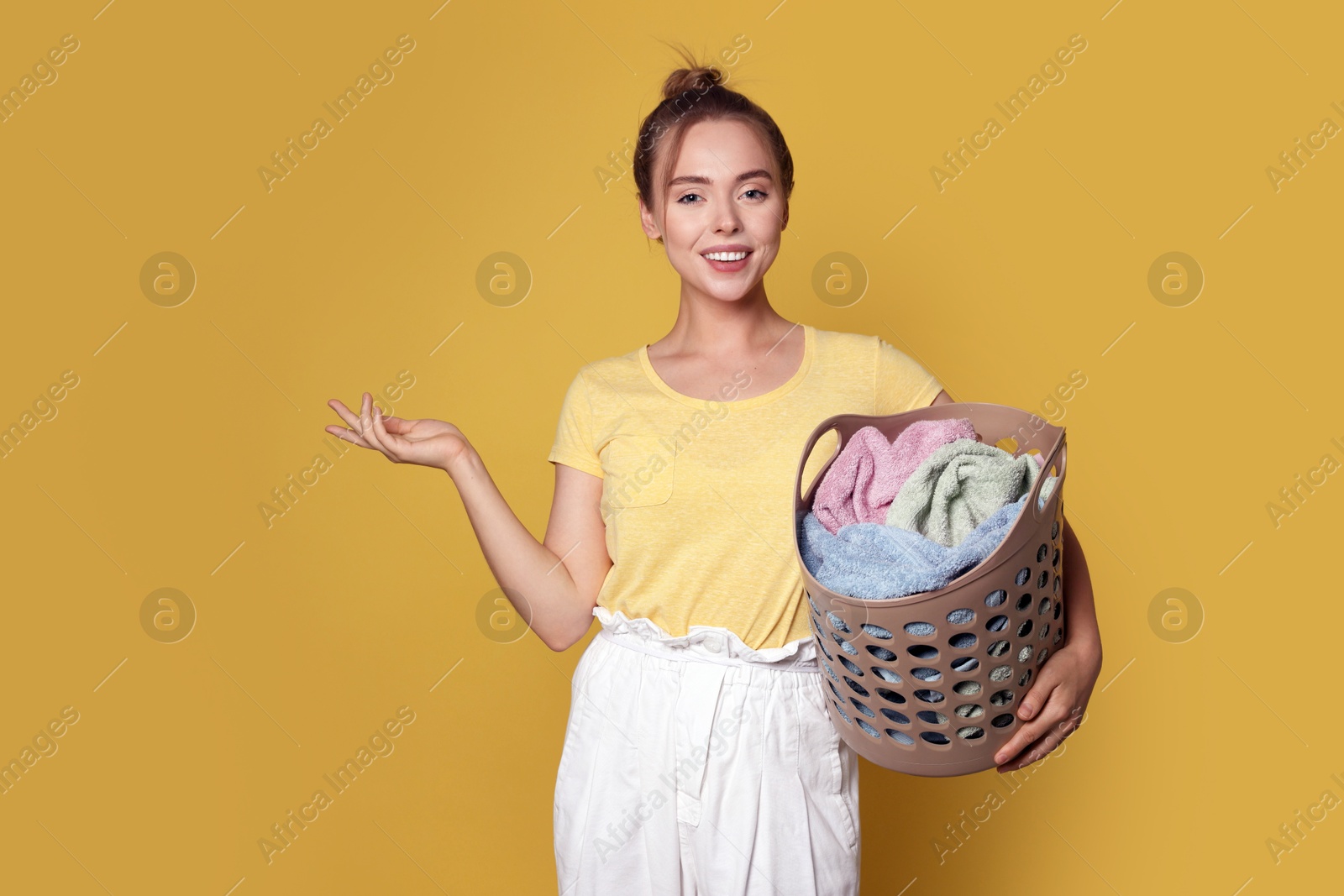 Photo of Happy young housewife with basket full of laundry on yellow background. Space for text