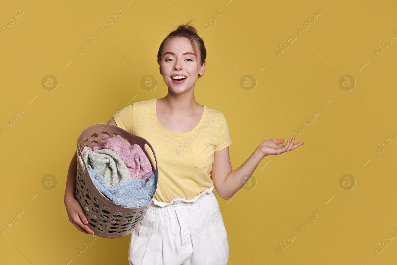 Photo of Happy young housewife with basket full of laundry on yellow background