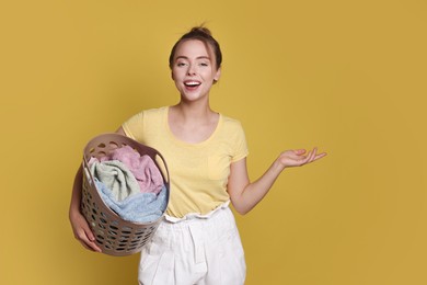 Happy young housewife with basket full of laundry on yellow background