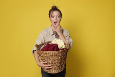 Emotional housewife with basket full of laundry on yellow background