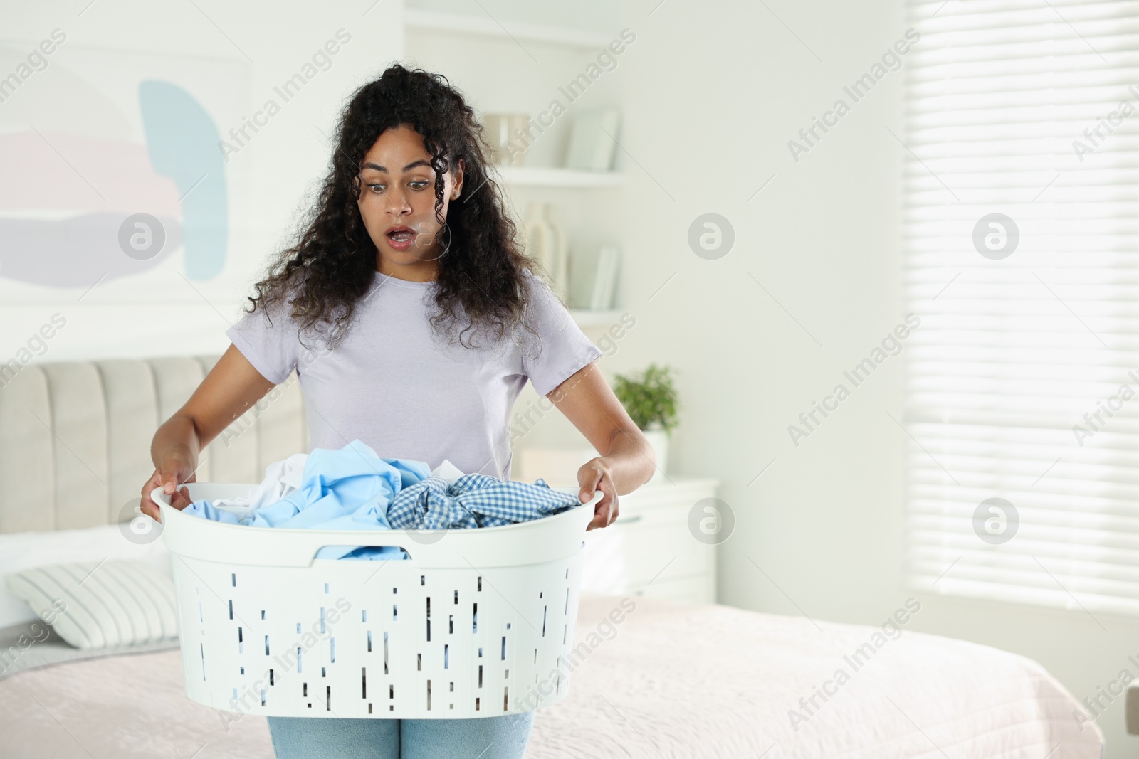 Photo of Shocked woman with basket full of laundry in bedroom, space for text