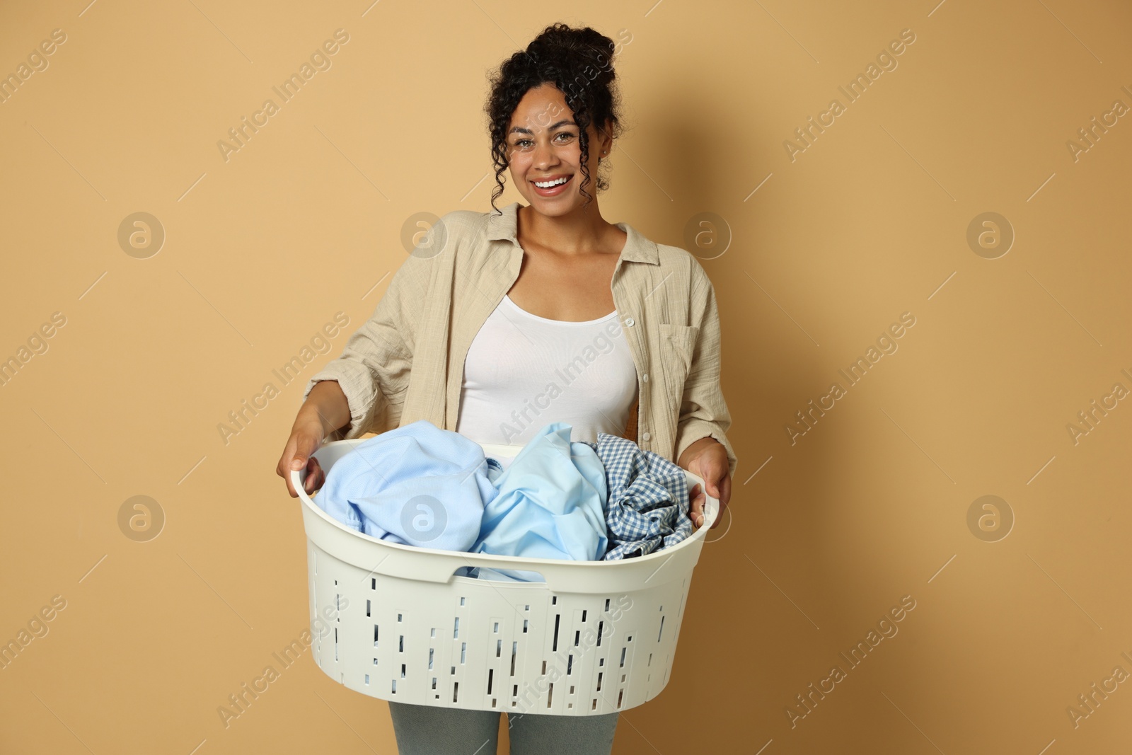 Photo of Happy woman with basket full of laundry on beige background