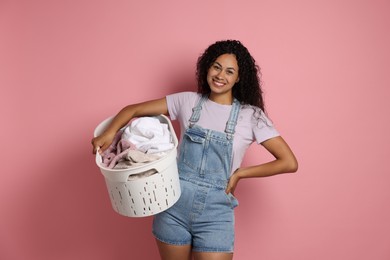 Photo of Happy woman with basket full of laundry on pink background