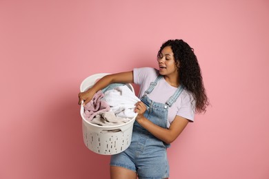 Photo of Happy woman with basket full of laundry on pink background