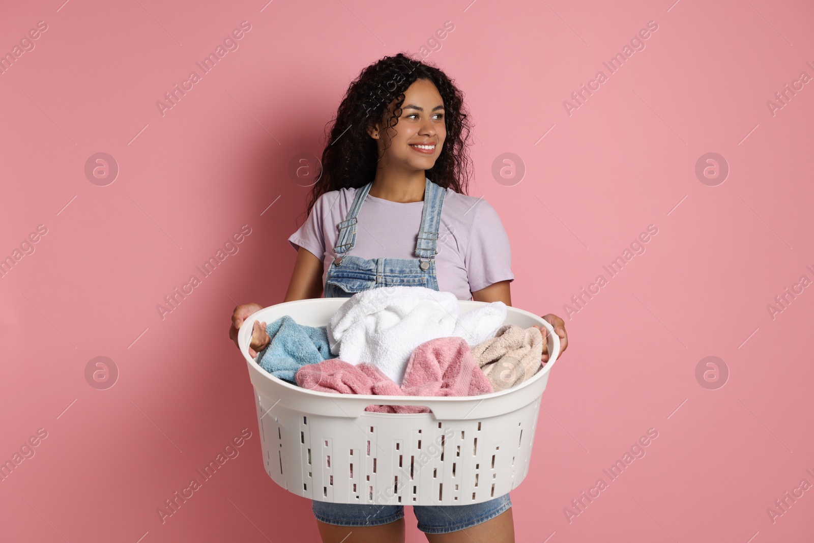 Photo of Happy woman with basket full of laundry on pink background