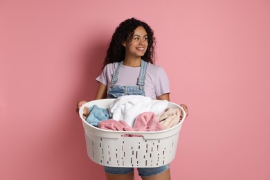 Happy woman with basket full of laundry on pink background