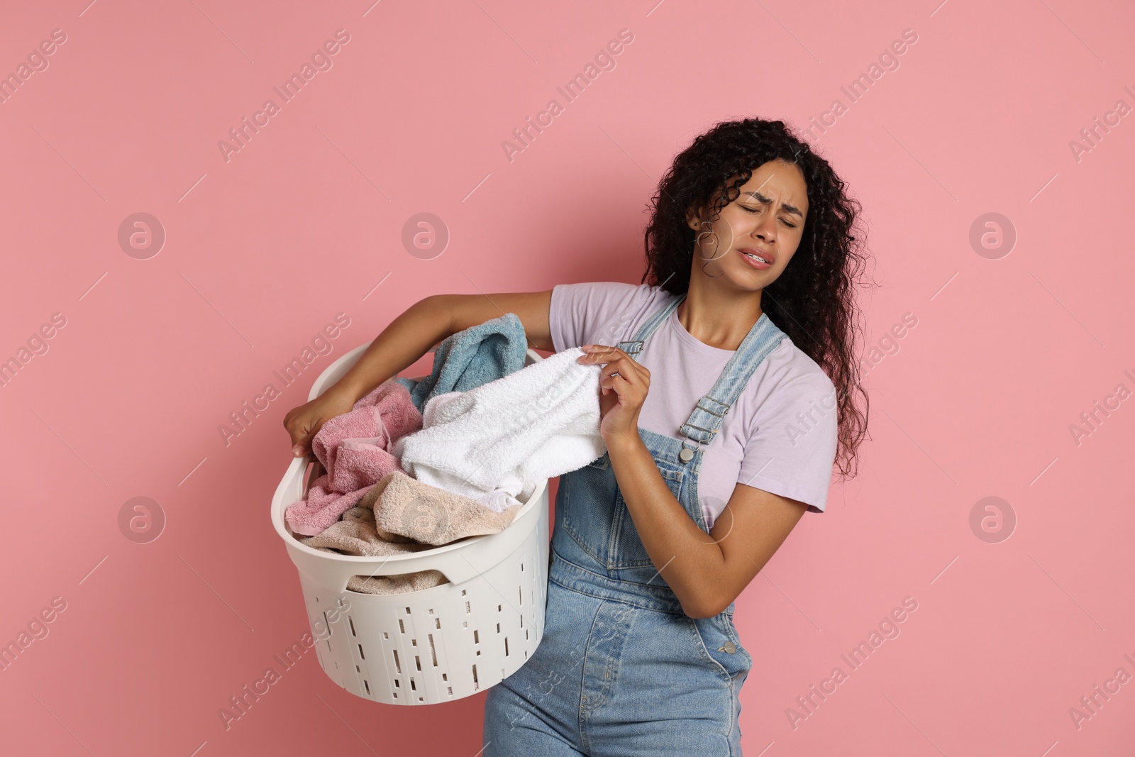 Photo of Displeased woman with basket full of laundry on pink background