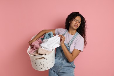 Photo of Displeased woman with basket full of laundry on pink background