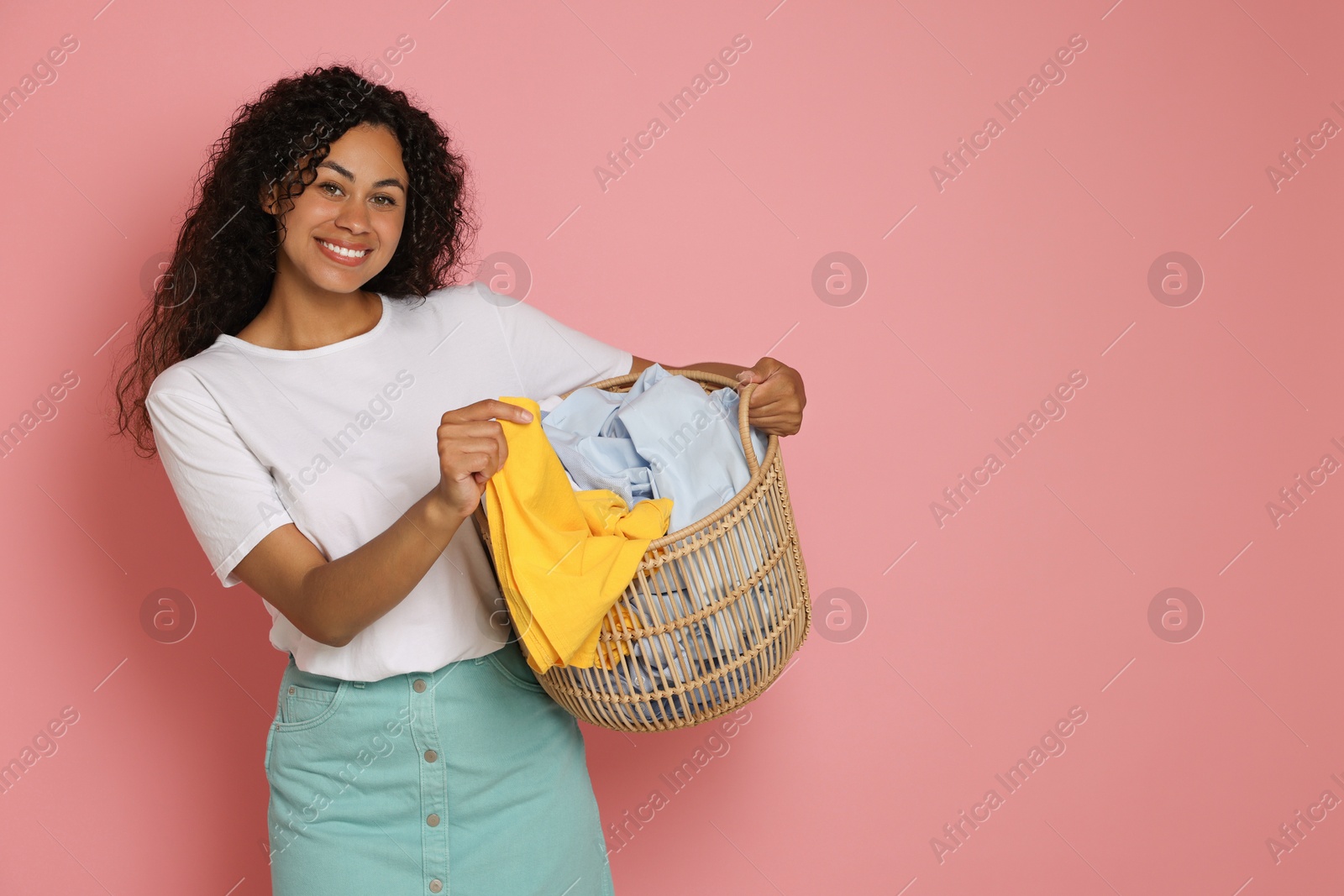 Photo of Happy woman with basket full of laundry on pink background, space for text