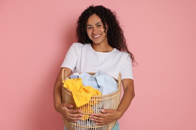 Happy woman with basket full of laundry on pink background