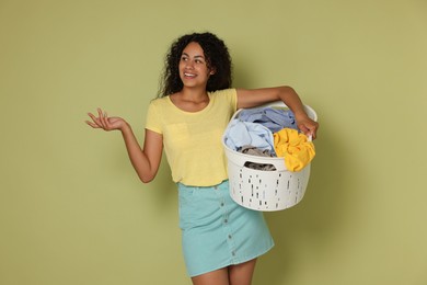 Happy woman with basket full of laundry on olive background