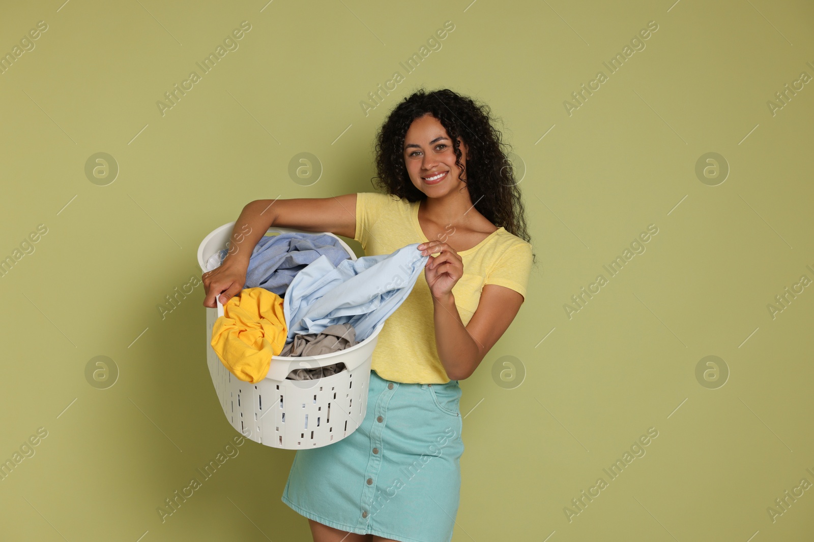 Photo of Happy woman with basket full of laundry on olive background