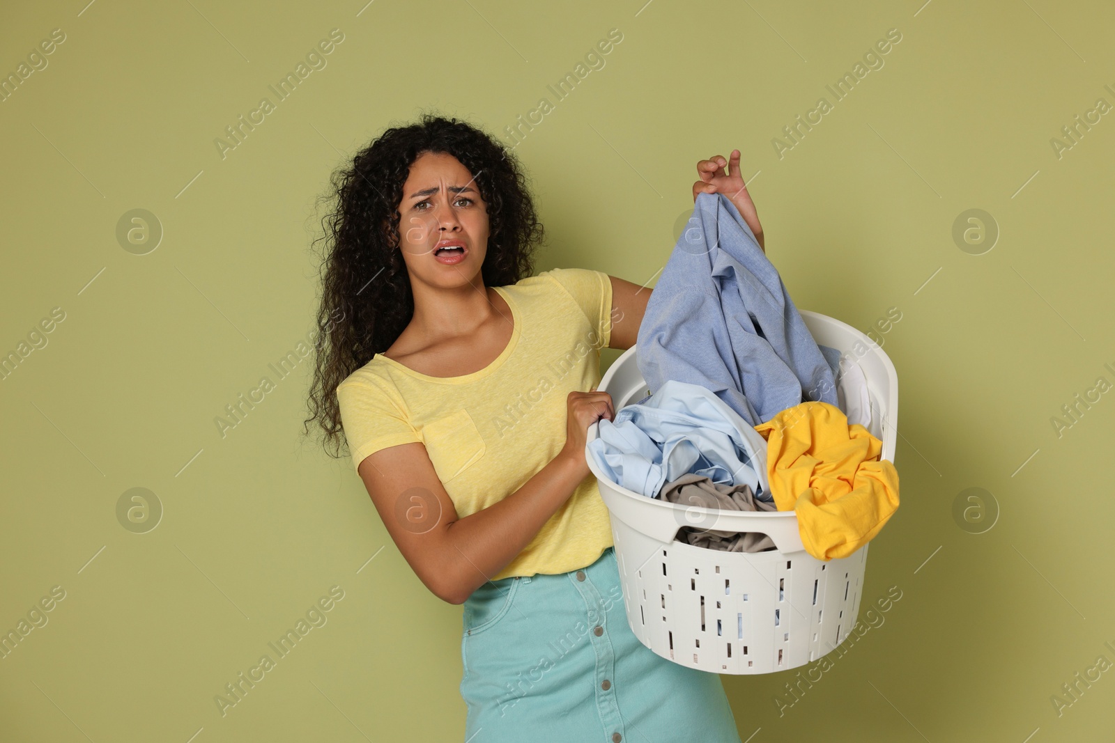 Photo of Displeased woman with basket full of laundry on olive background