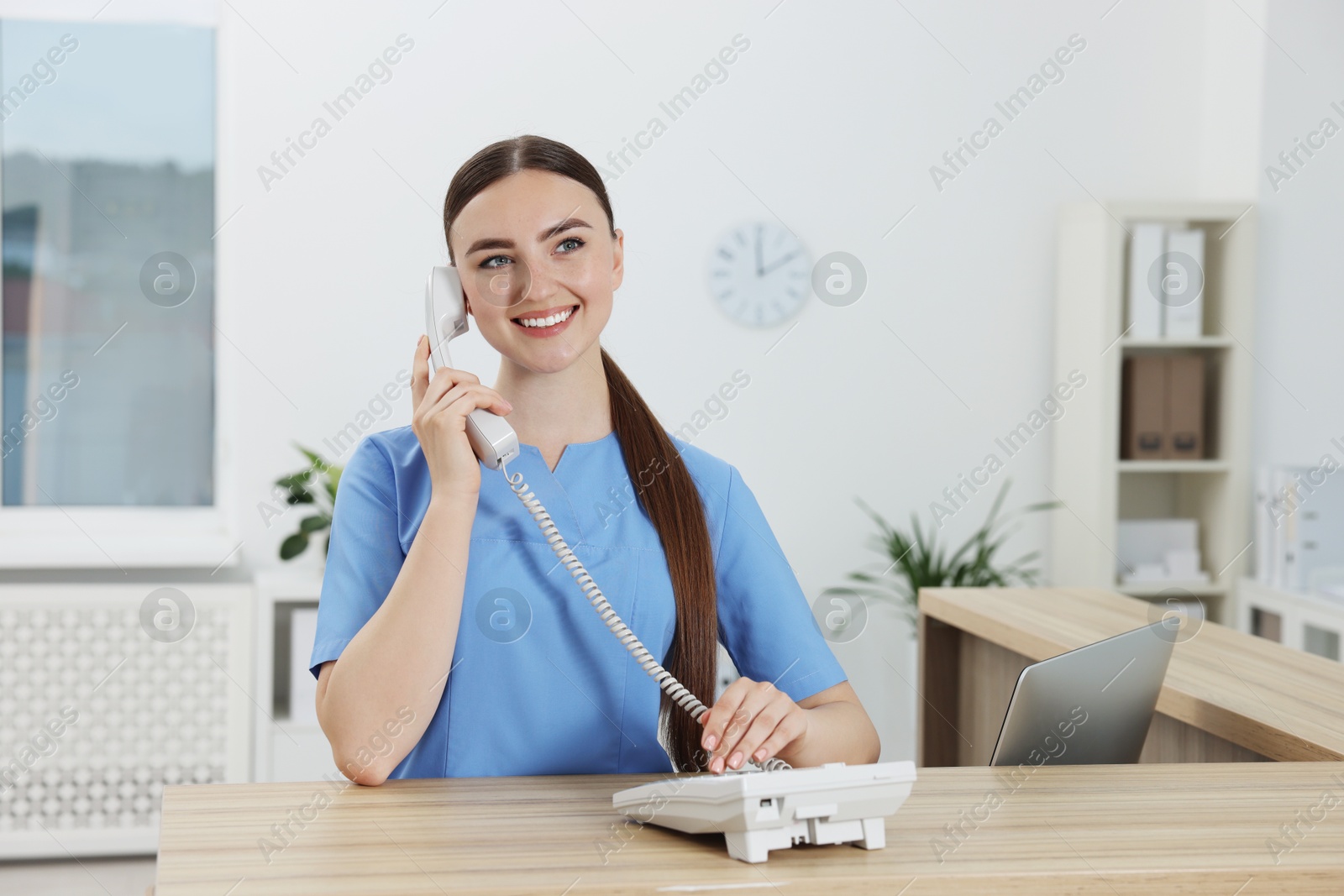 Photo of Professional receptionist talking on phone at wooden desk in hospital