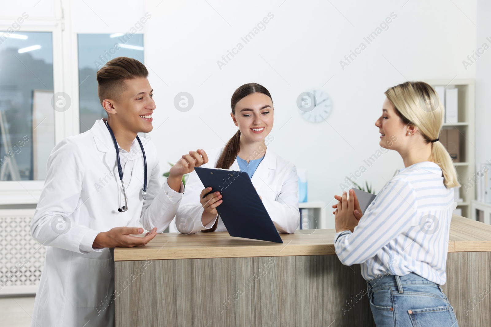 Photo of Professional receptionist and doctor working with patient at wooden desk in hospital