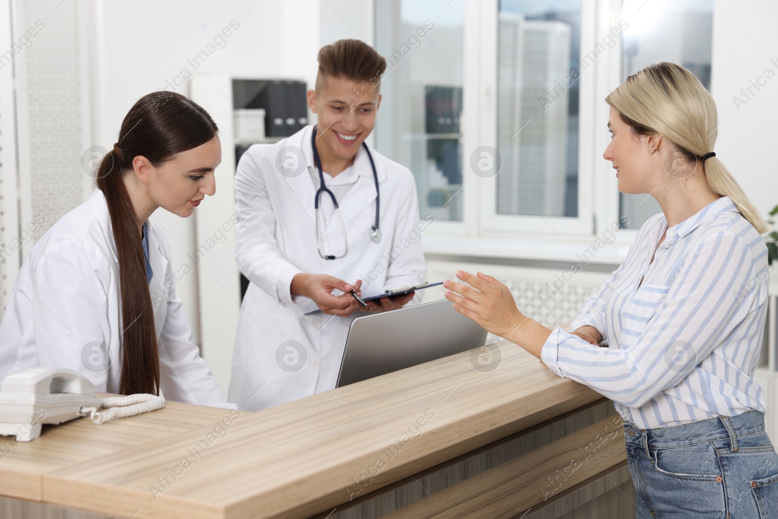 Photo of Professional receptionist and doctor working with patient at wooden desk in hospital