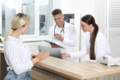 Professional receptionist and doctor working with patient at wooden desk in hospital