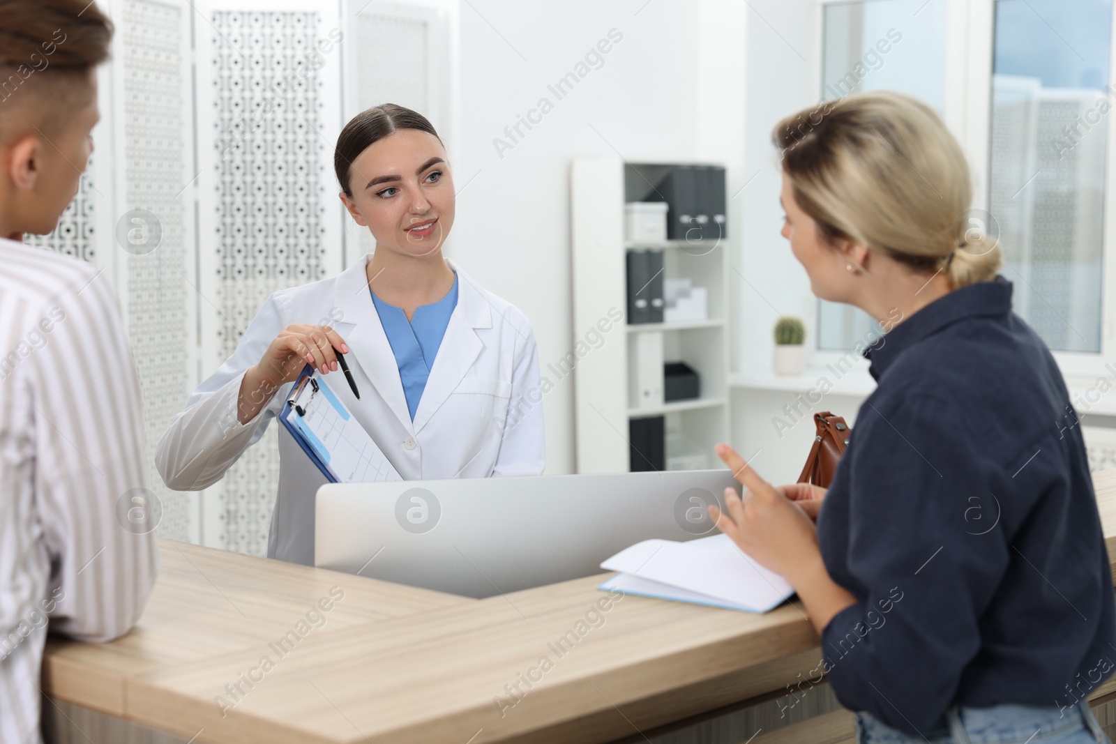 Photo of Professional receptionist working with patients at wooden desk in hospital