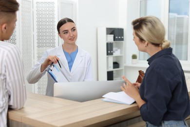 Photo of Professional receptionist working with patients at wooden desk in hospital