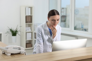 Professional receptionist working at wooden desk in hospital