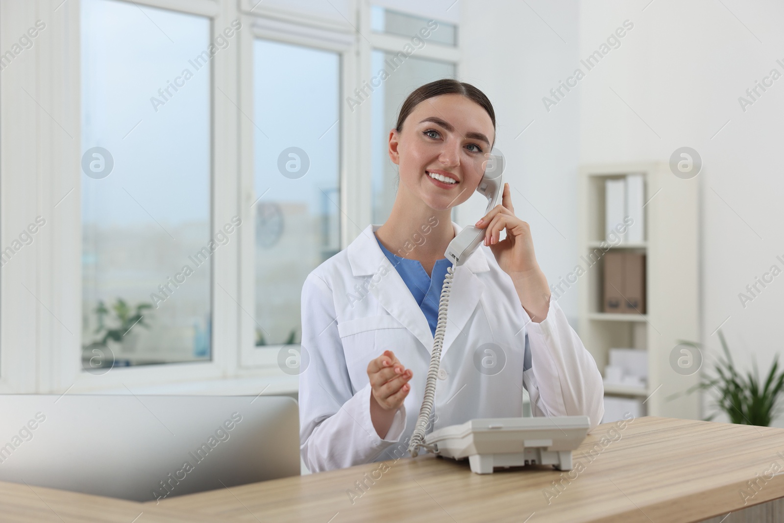 Photo of Professional receptionist talking on phone at wooden desk in hospital