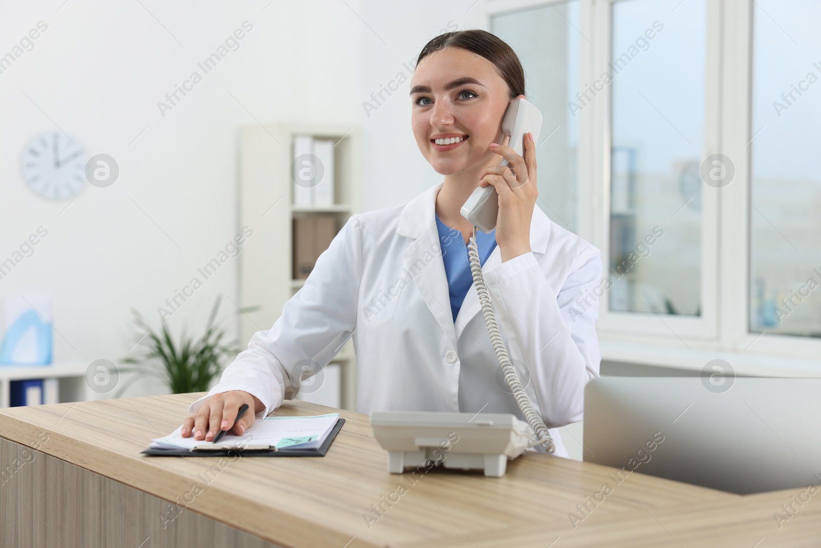 Photo of Professional receptionist talking on phone at wooden desk in hospital